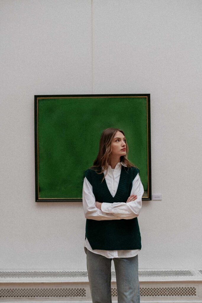 Outfit složený z tmavě zelené vesty, bílé košile a světlých džínů.