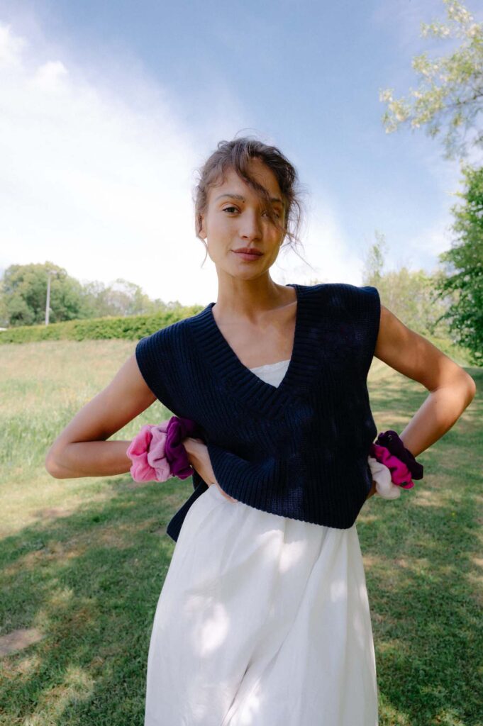 Žena v tmavě modré vestě a bílých šatech stojí venku.